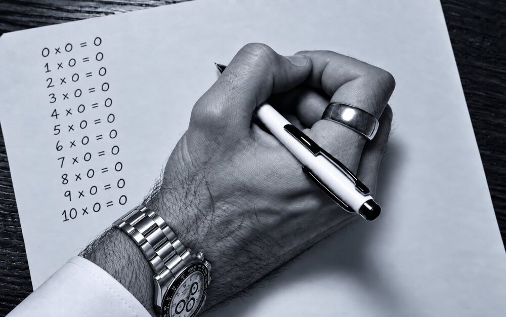 Una mano scrive a penna la tabellina dello zero, da 0x0=0 a 10x0=0, su un foglio bianco